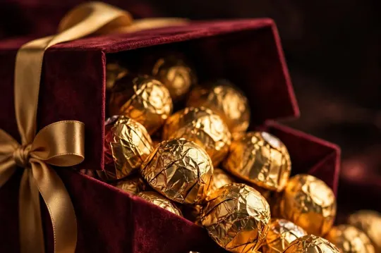 Burgundy velvet box overflowing with gold-wrapped chocolates
